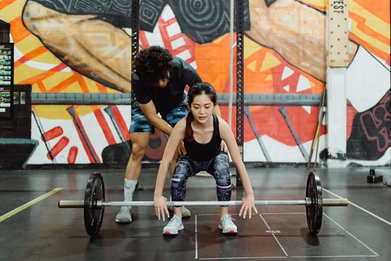 Woman lifting weights with a trainer in a gym, promoting fitness and strength.