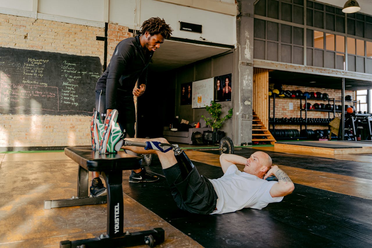 Man with prosthetic leg doing crunches in gym with personal trainers support.